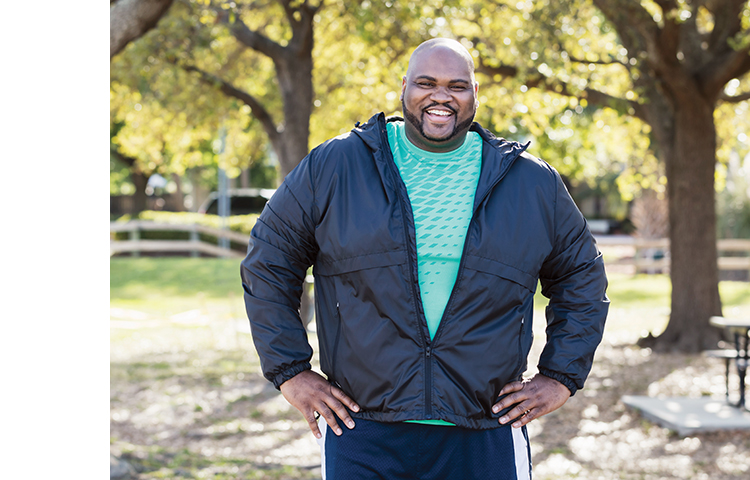 Overweight man standing outdoors in a park.