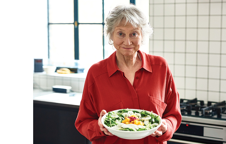Person in kitchen holding a bowl of salad.