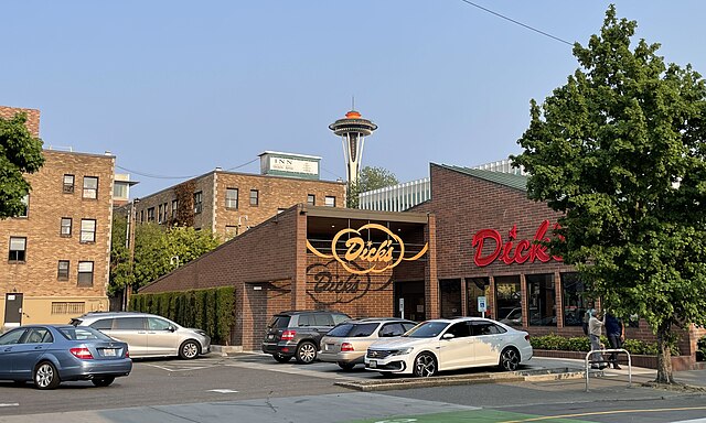  A busy street scene in Seattle's Capitol Hill with pedestrians crossing, cyclists in dedicated bike lanes, and cars and a streetcar at a red light. Shops and restaurants line the street, and a sign indicates turning vehicles must stop for pedestrians and cyclists. The area accommodates multiple forms of transportation.