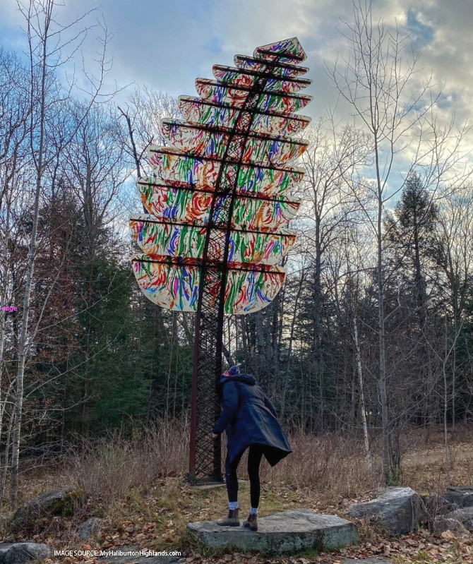  A person looks up at a towering fern sculpture made of metal and brightly colored panels. 