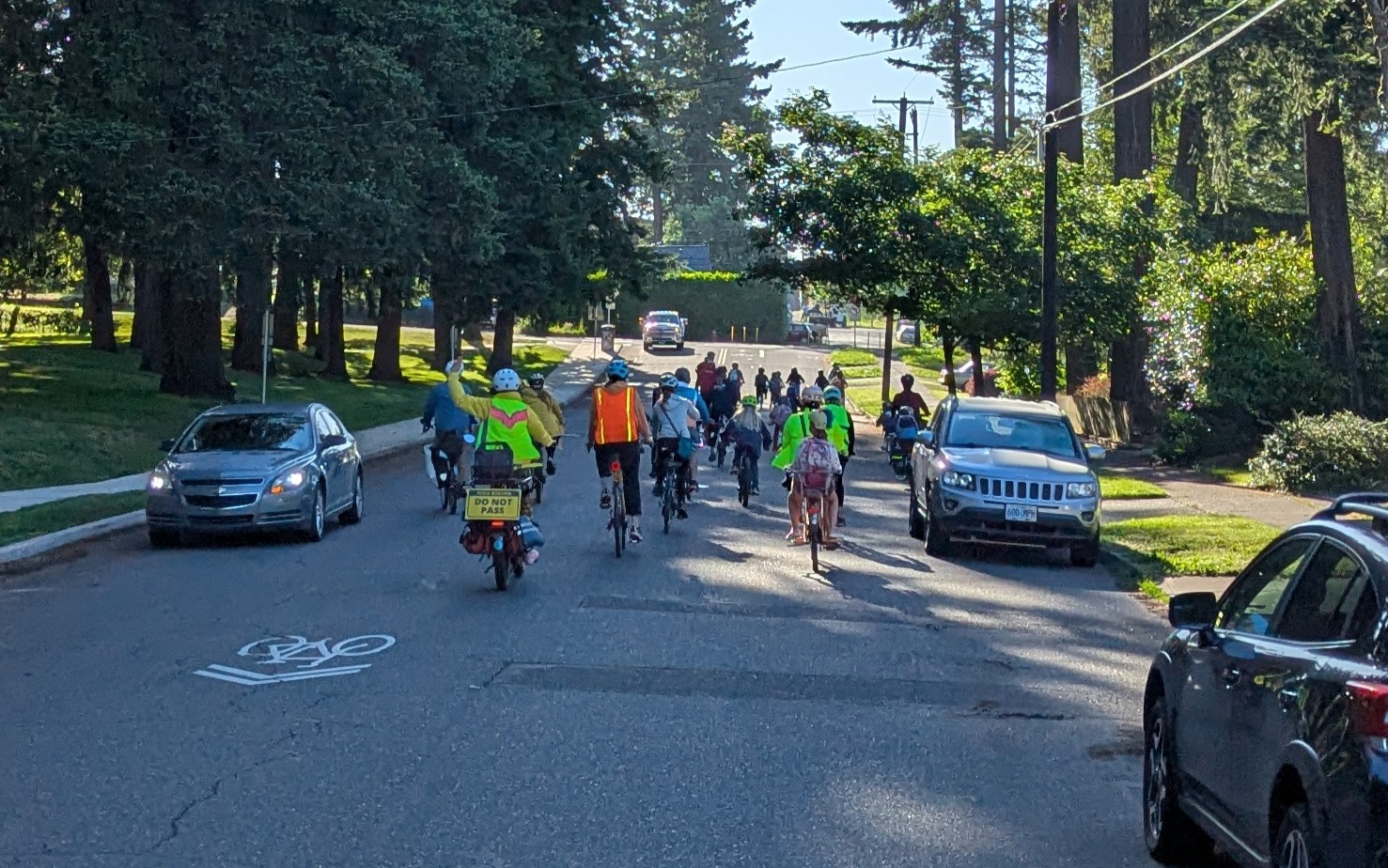 the Lent bike bus on the way to school. they bike down a shady street as they approach the crossing of SE 92nd Ave on Steele.