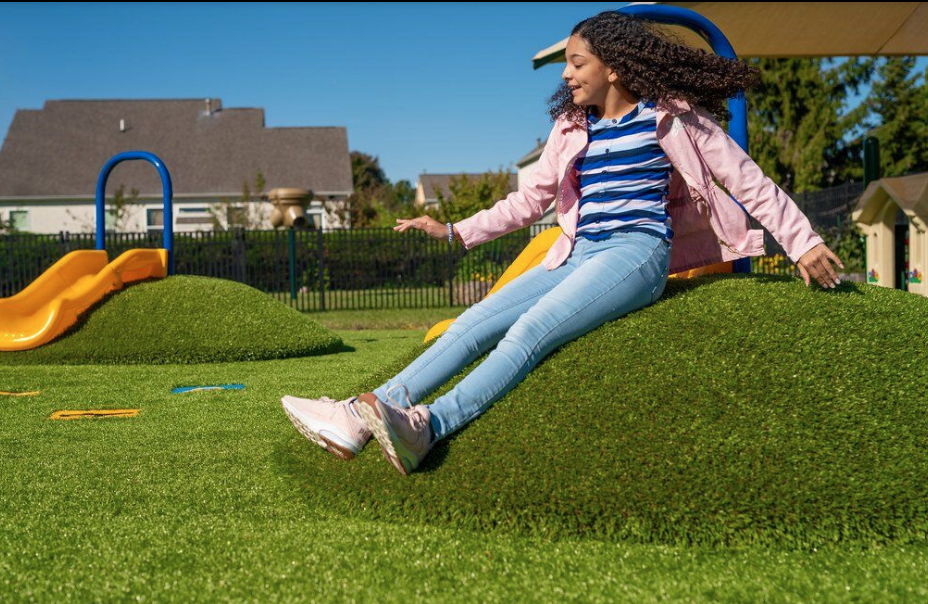 Child playing on grass mound play feature