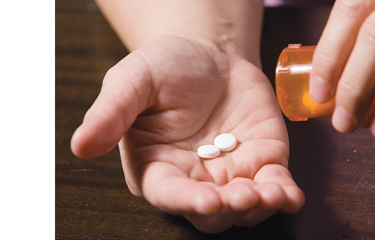 Close-up of hand pouring two pills from medicine bottle into other hand.