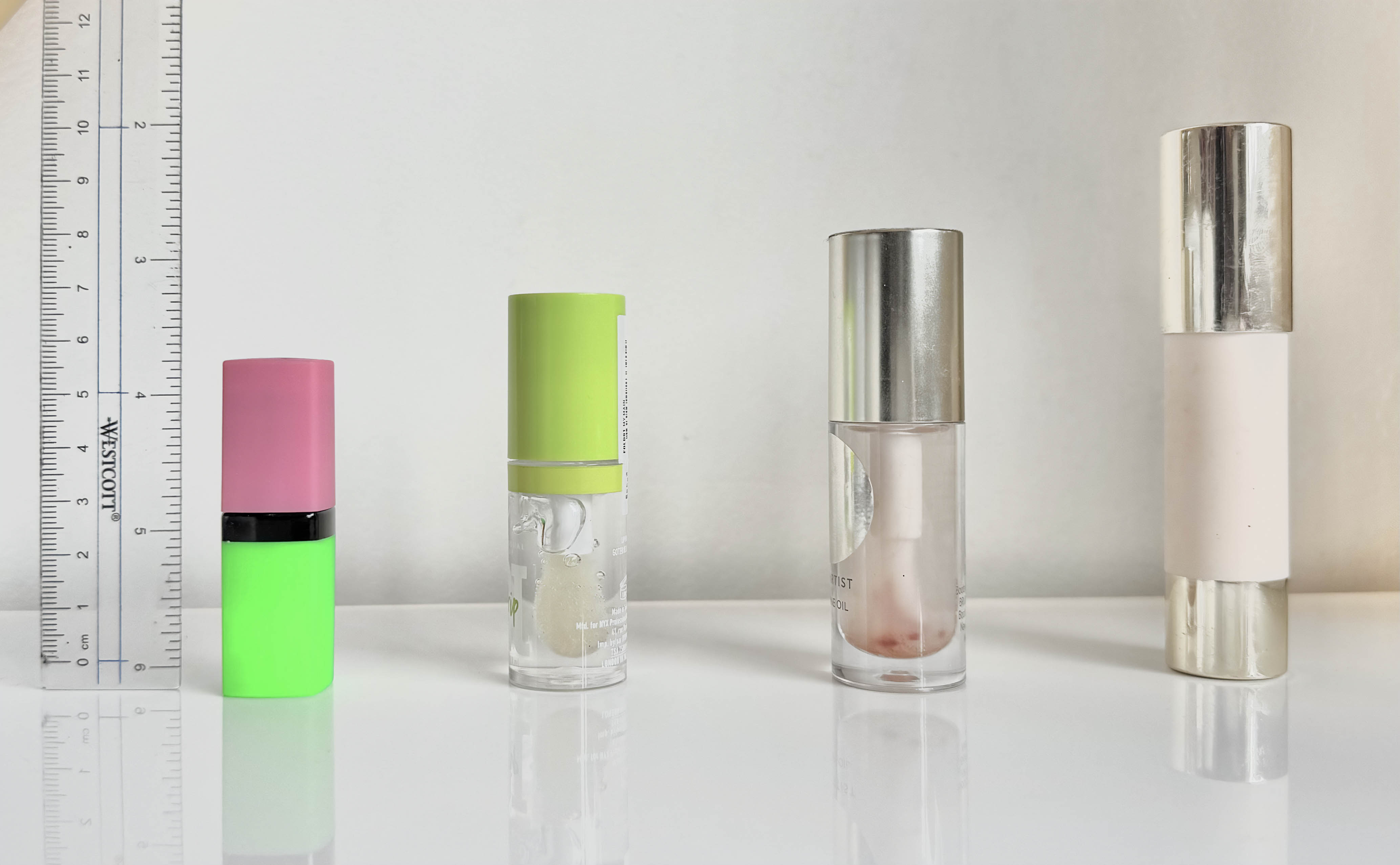 4 makeup bottles lined up in ascending order of size with a ruler to the left for scale. Each product will be described in the answers below