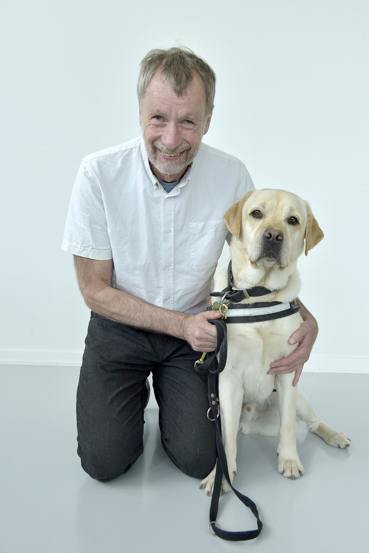 Pluto er en lys labrador. Her sidder han ved siden af Michael, som sidder på knæ og holder om Pluto. 