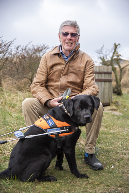 Siffi er en sort labrador. Her sidder hun foran Hans Verner iført sin førerhundebøjle.  