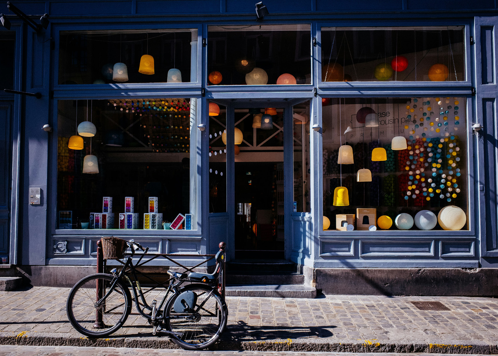 A storefront with blue walls, large windows, lanterns, and a bike upfront.