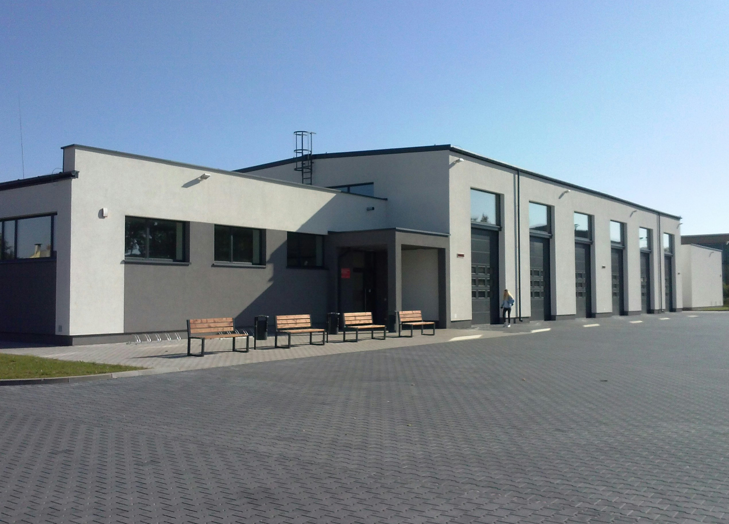 A large, grey warehouse with large doors near empty pavement.